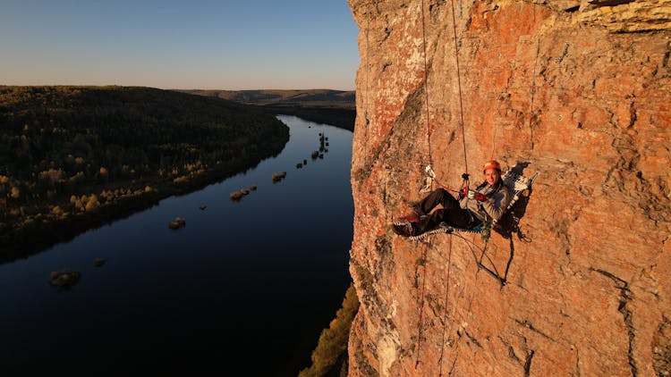 A Woman Sitting On A Chair Hanging From A Mountain Cliff