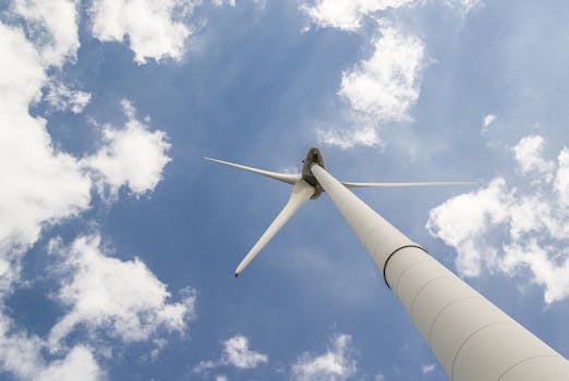 View of a towering wind turbine against a cloudy blue sky, highlighting renewable energy technology.