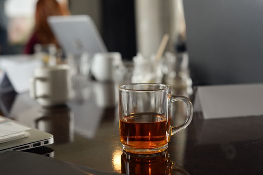 A clear glass mug of tea on a reflective table in an office setting, creating a warm atmosphere.