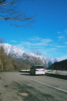 White van on a scenic mountain highway under a clear blue sky with snow-capped peaks.