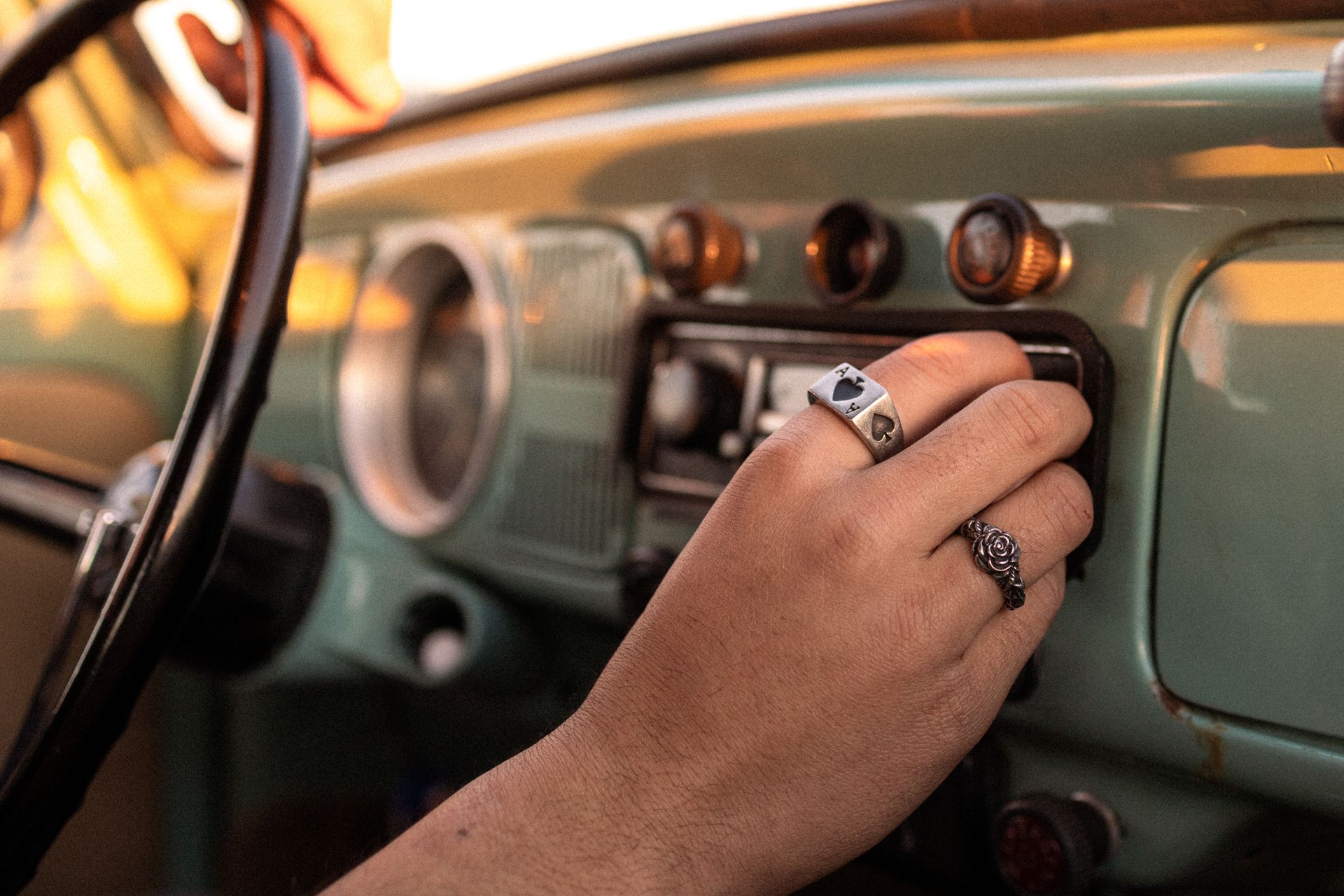 Close-up of hand adjusting radio in a vintage car. Sunlit atmosphere, intricate rings on fingers.