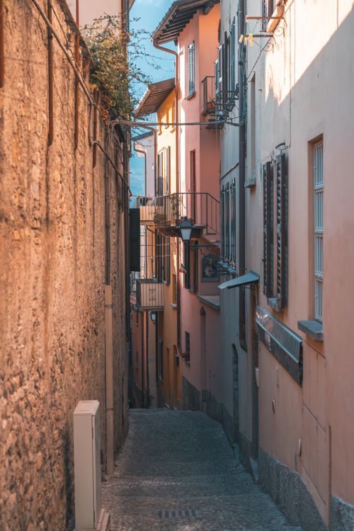 Free Explore a narrow European alleyway bathed in warm light, featuring colorful buildings and serene architecture. Stock Photo