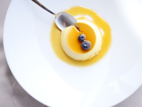 Flat lay of a pudding topped with blueberries and syrup, elegantly presented on a white plate.