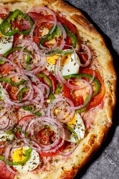 Close-up of a colorful vegetable pizza topped with sliced eggs and herbs on a stone surface.