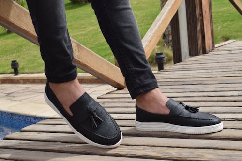 무료 술이 달린 흰색과 검은 색 가죽 슬립 온 신발을 신고있는 사람 스톡 사진