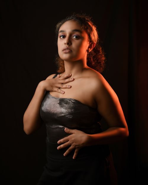 Free Young woman elegantly poses in a stylish black dress against a dark studio background. Stock Photo