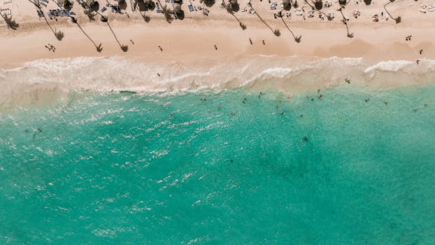 Drone view of a lively beach with turquoise waters and sunbathing tourists, perfect for a summer getaway.