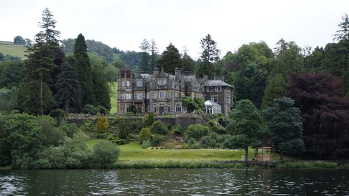 Free Charming historic castle surrounded by lush gardens and a tranquil lake, perfect for travel and nature enthusiasts. Stock Photo