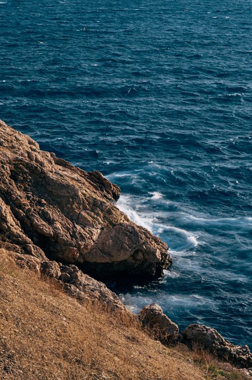 Free High-angle view of a rocky coast with waves crashing against rugged cliffs and a deep blue sea. Stock Photo