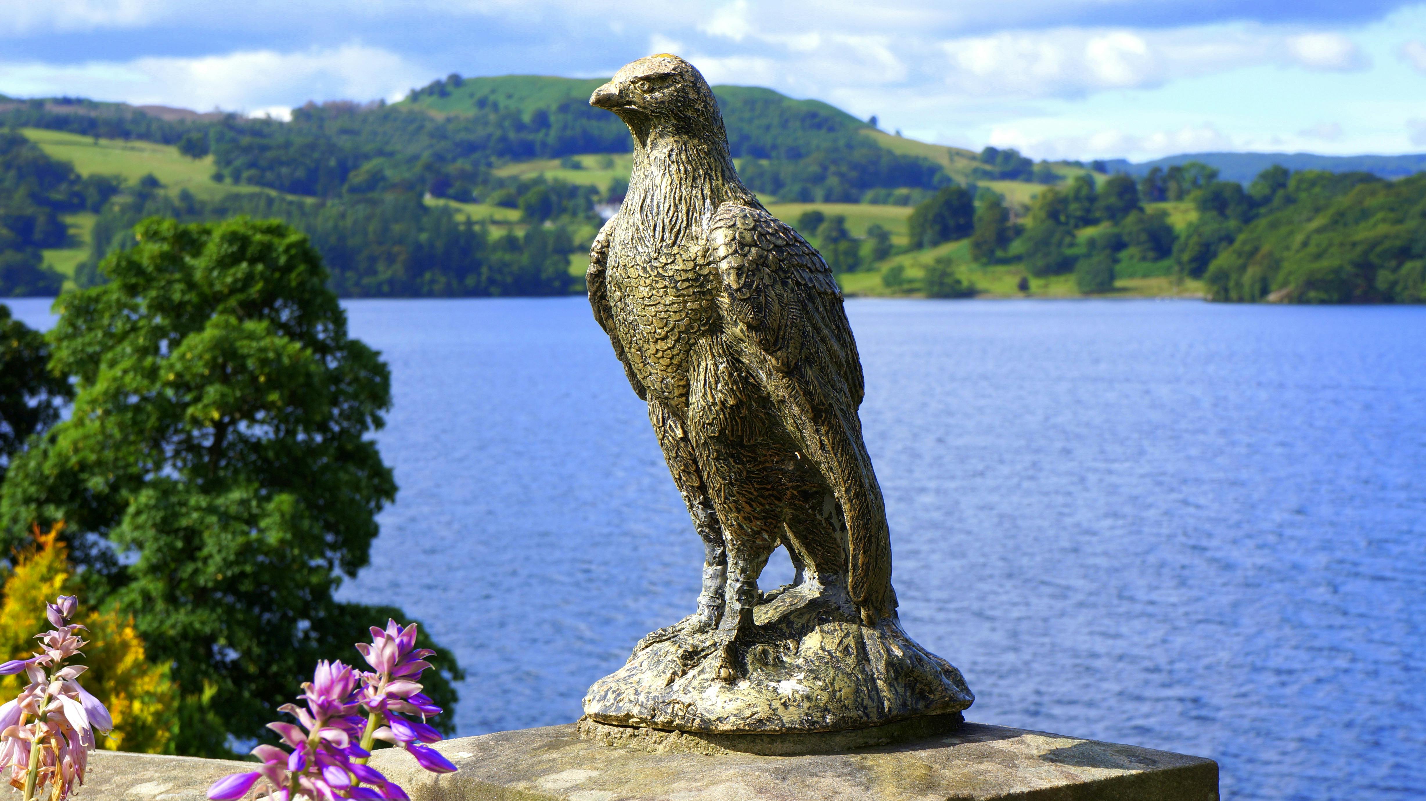 在明亮的天空下，鹰雕塑俯瞰着宁静的湖泊和郁郁葱葱的青山