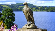 在明亮的天空下，鹰雕塑俯瞰着宁静的湖泊和郁郁葱葱的青山