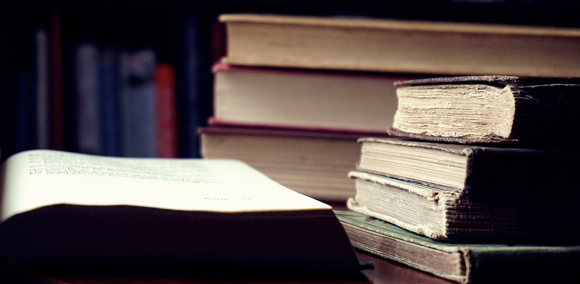 A stack of vintage hardcover books in a dimly lit library setting symbolizes knowledge and wisdom.