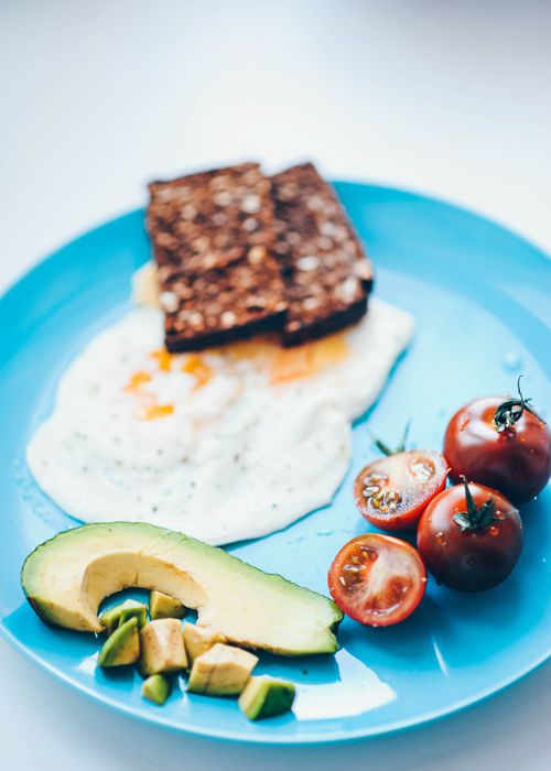 Free Delicious and nutritious breakfast of fried eggs, avocado, and cherry tomatoes on a blue plate. Stock Photo