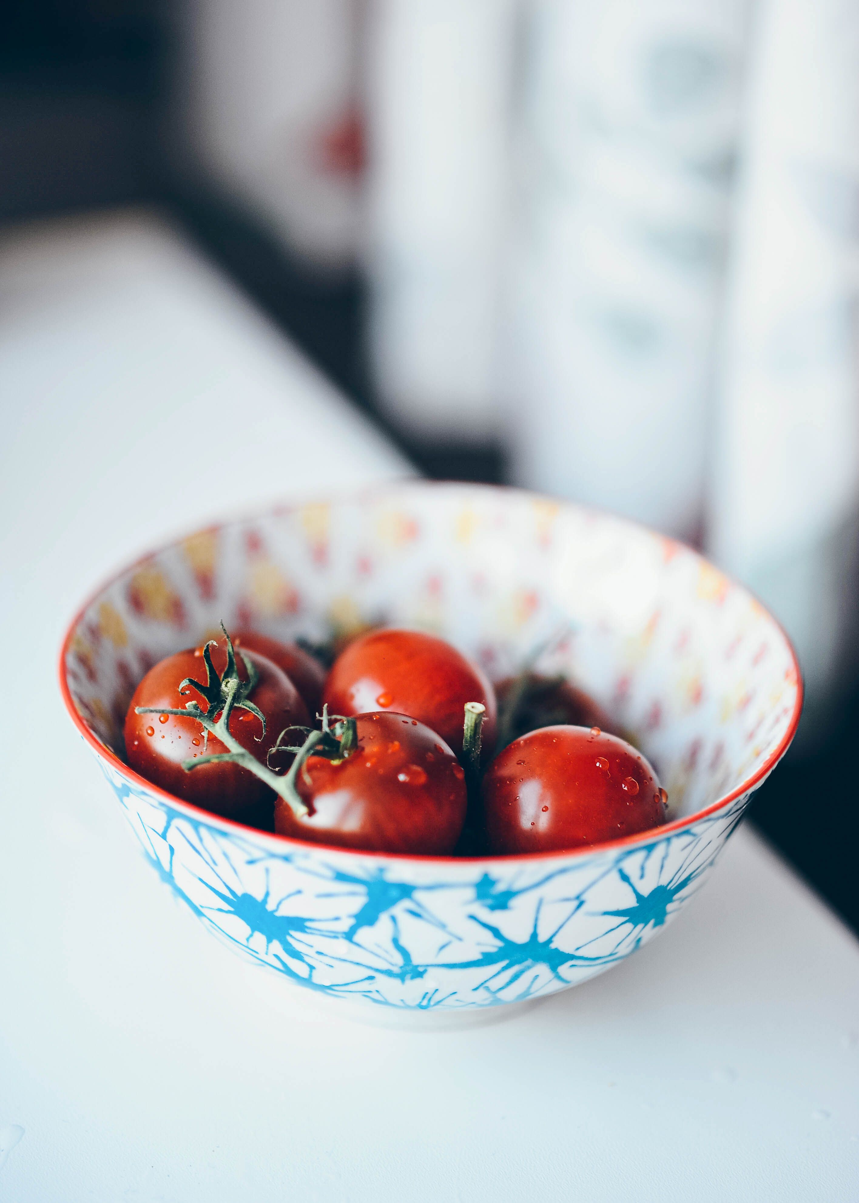 Vibrant cherry tomatoes in a patterned bowl on a white surface, perfect for food photography.