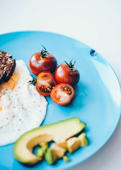 Delicious breakfast featuring fried eggs, cherry tomatoes, avocado, and rye bread on a blue plate.