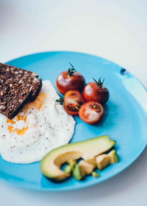 Free A close-up of a nutritious breakfast with sliced avocado, poached eggs, tomatoes, and rye bread. Stock Photo