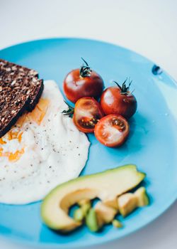 Delicious and nutritious breakfast plate featuring sunny side up egg, fresh tomatoes, avocado, and whole grain toast.