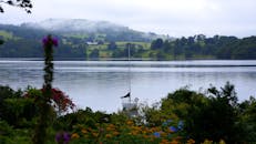 湖面风景如画，一艘帆船静静地停泊，四周环绕着鲜花和山丘