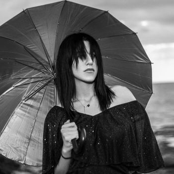 Artistic black and white portrait of a woman holding an umbrella by the sea, exuding elegance.