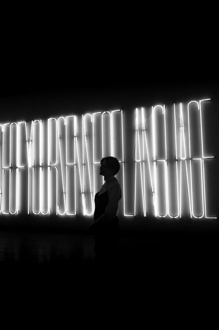 Silhouette of a woman against a bright neon sign in an Aarhus gallery creates a dramatic scene.