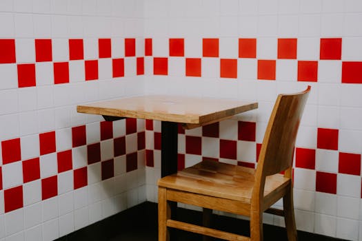 Wooden chair and table in a minimalistic corner with red and white checkered tiles.