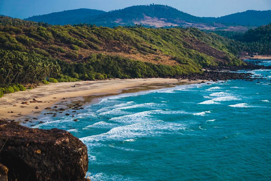 Breathtaking view of a serene beach with crashing waves and lush green hills.