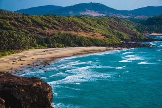 Breathtaking view of a serene beach with crashing waves and lush green hills.