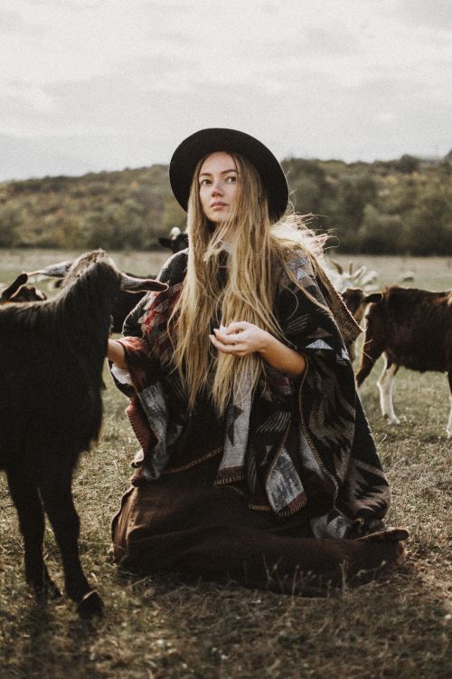 Free Woman wearing poncho and hat, surrounded by goats in a serene outdoor setting. Stock Photo
