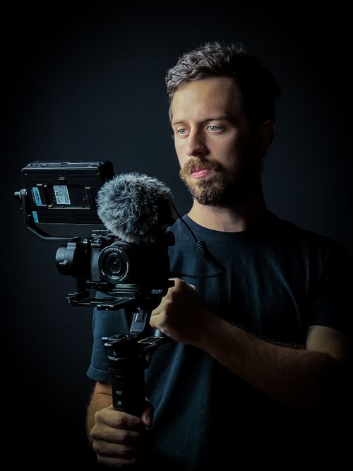 Free A bearded videographer holding a camera rig during a studio photoshoot. Stock Photo