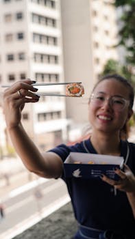 Smiling woman holding sushi with chopsticks on an urban street.