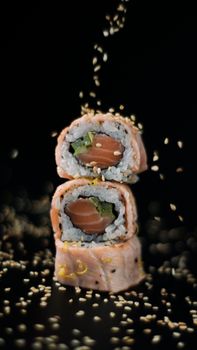 Close-up of delicious sushi rolls with sesame seeds falling, showcasing Japanese culinary art.