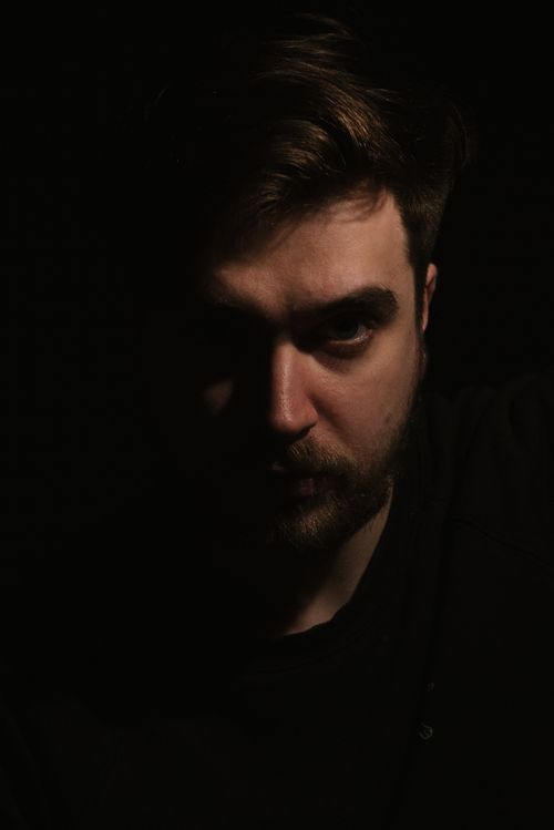Free Intense low-key portrait capturing a man with dramatic half face shadow in a dark studio setting. Stock Photo