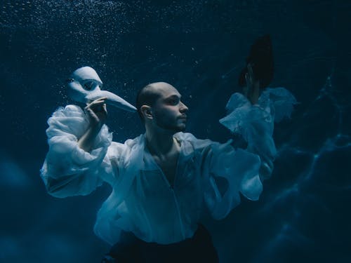 Man in Shirt Posing Underwater and Holding Theatre Mask 