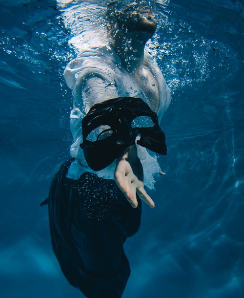 Free A person reaching underwater while holding a black mask in a dramatic scene. Stock Photo
