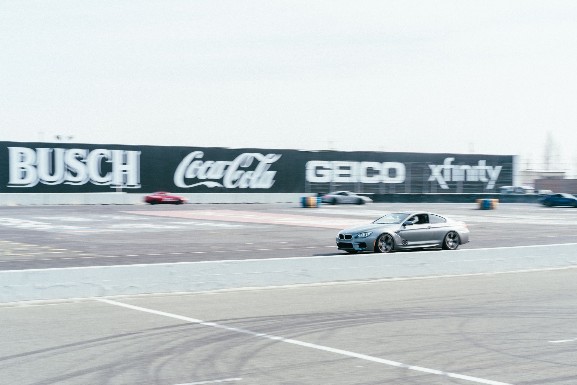 A sleek silver car speeds around a race track under a clear sky.