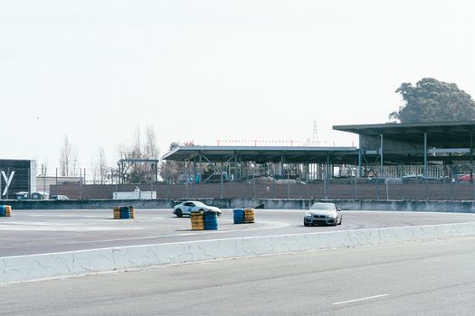 Cars racing on an urban track with empty stands and a clear sky.