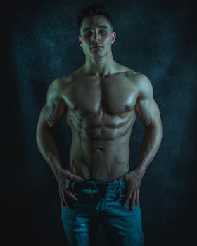 A fit and muscular Caucasian male posing shirtless in a moody studio shoot.