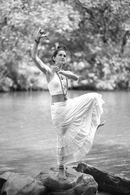 A woman elegantly posing on a rock by the river in black and white.
