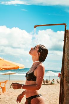 Young woman in bikini taking an outdoor shower on a sunny beach day, capturing the essence of summer relaxation.