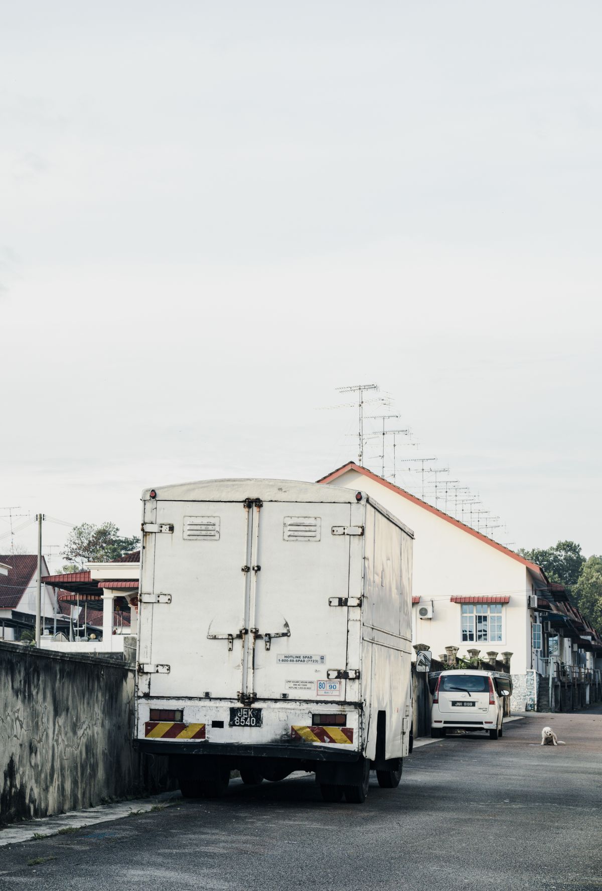 A plain white box-body lorry with no stickers parked on a Malaysian residential street — the blank surface before design and installation work begins