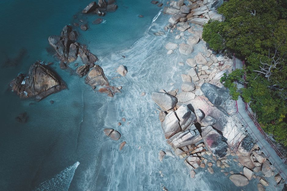 Vibrant aerial shot of a rocky beach with turquoise water and lush greenery, perfect for travel imagery.