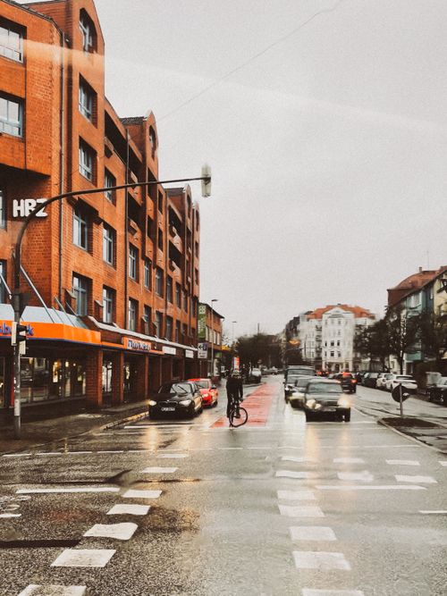 Free City street with vehicles and cyclist on a wet day, featuring red brick architecture. Stock Photo