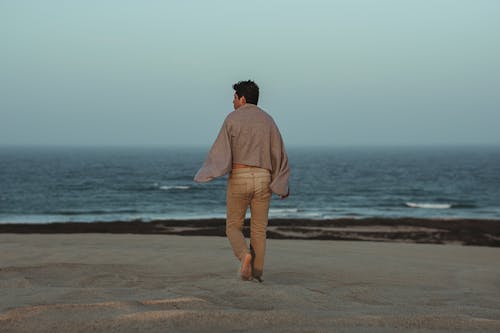 Man Walking Towards Shore With Grey Towel on Back