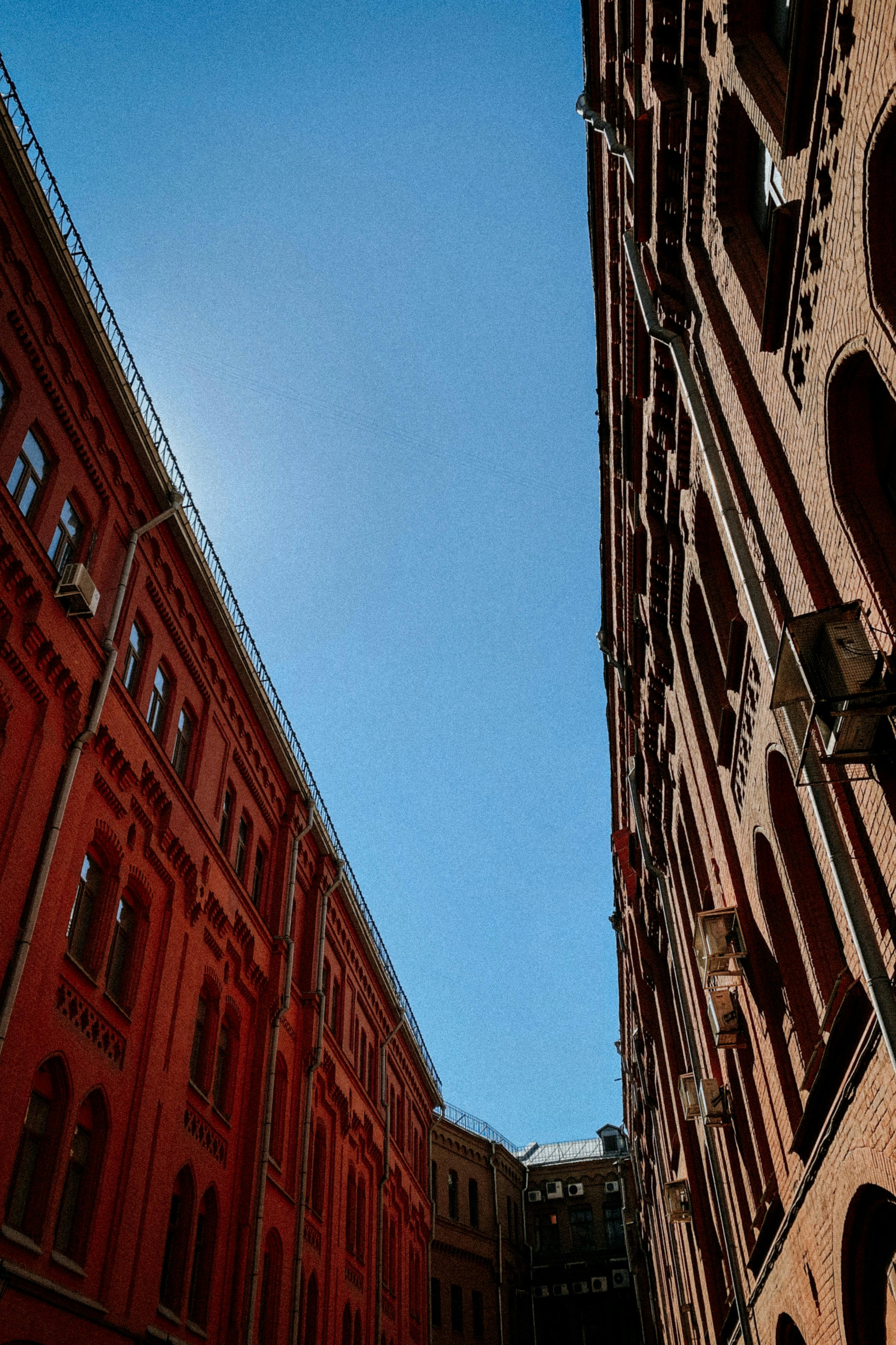 Low angle view of historic red brick buildings against a clear blue sky, showcasing urban architecture.