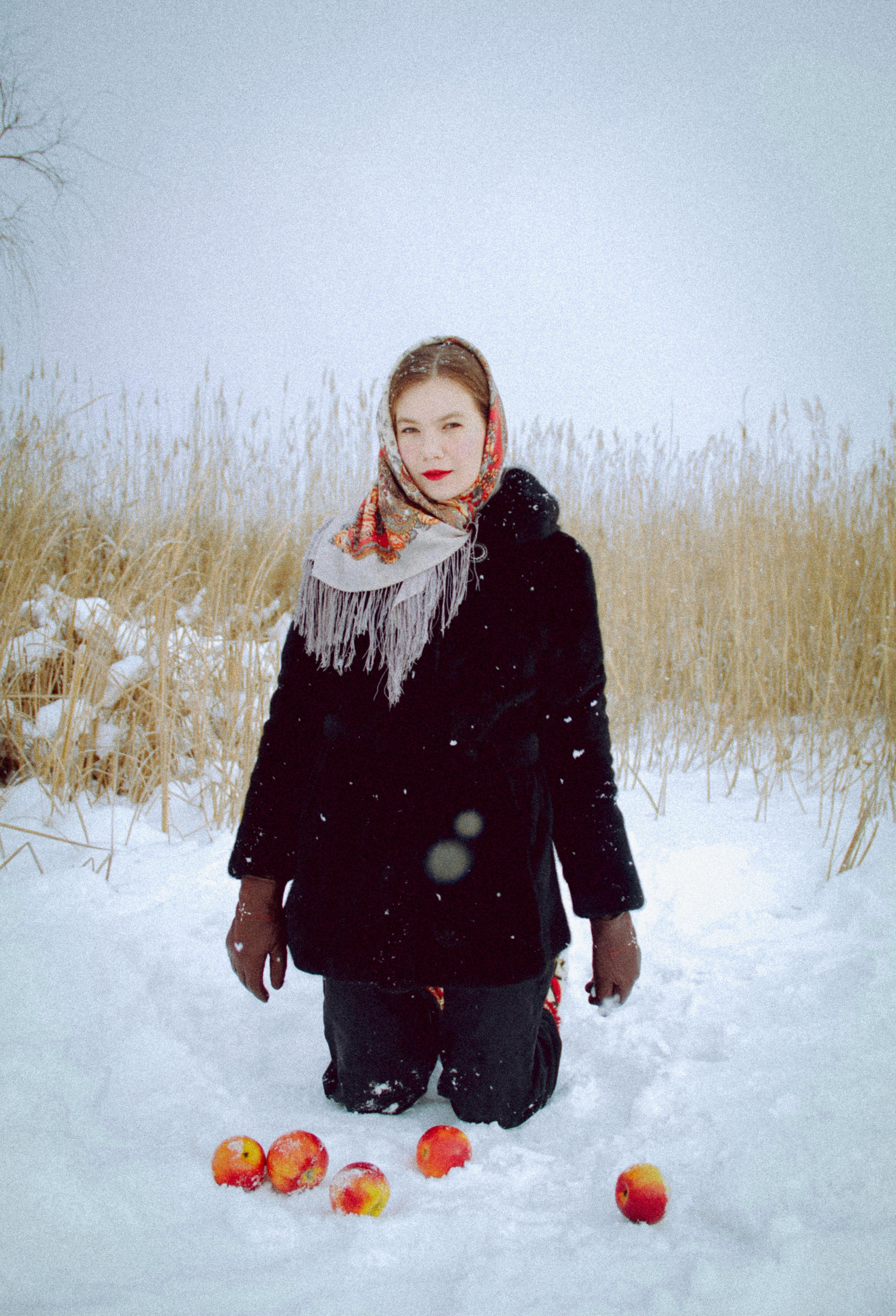A woman in a winter scene kneeling in snow with apples on the ground.