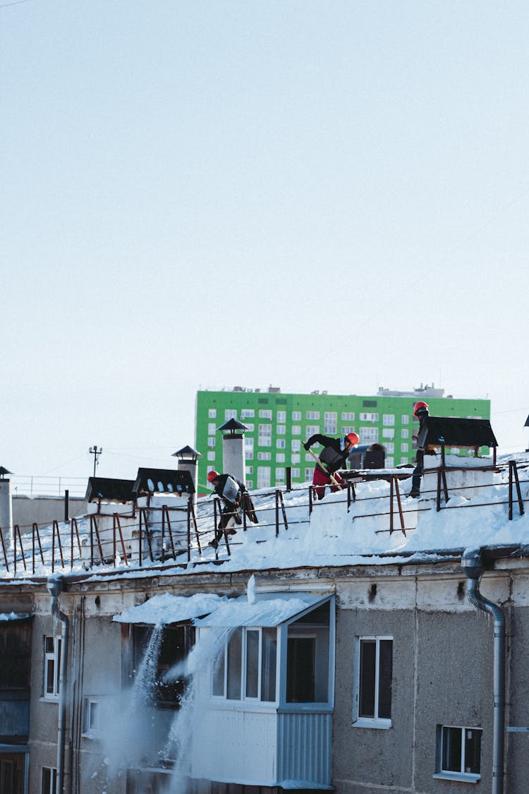 
People Shoveling Snow Off A Roof