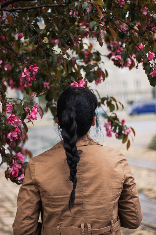 Free A woman with a braided hairstyle standing under a blooming tree in an urban setting. Stock Photo