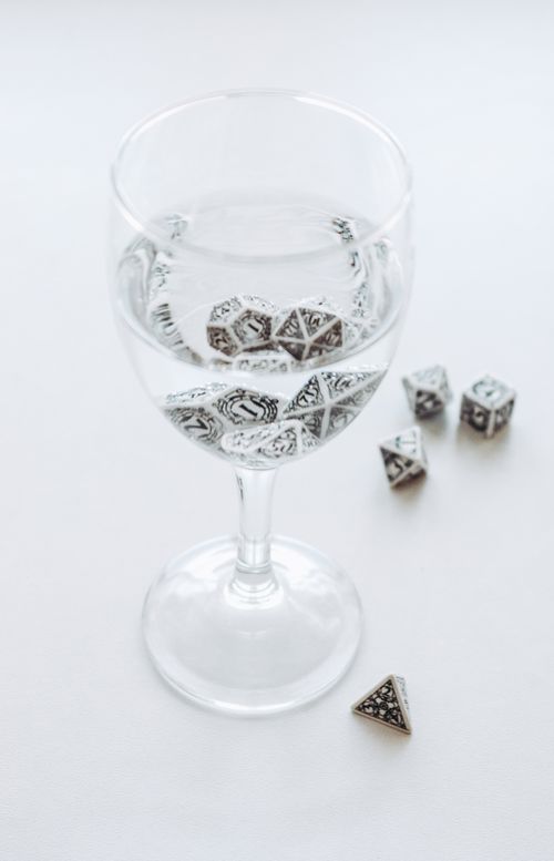 Free A glass of water containing beautifully patterned metallic dice, artistically arranged on a white surface. Stock Photo