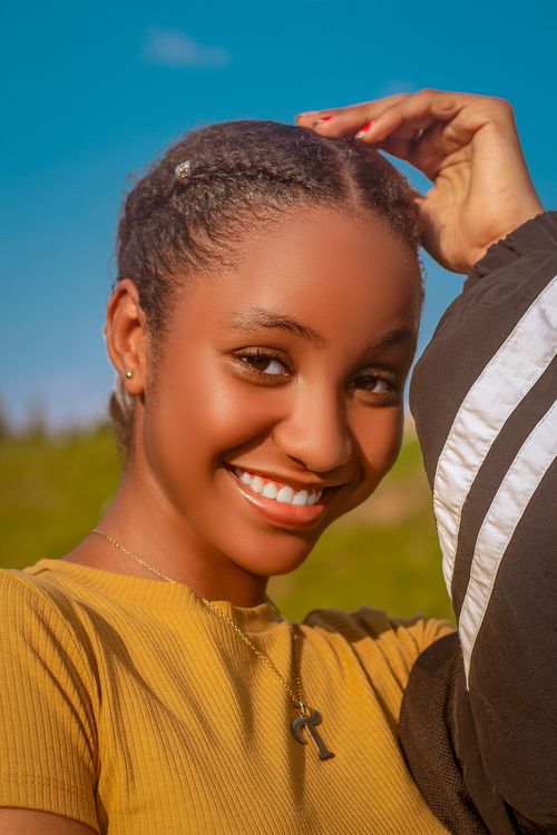 Free Close-up of a young woman with braided hair smiling against a clear blue sky, exuding happiness and warmth. Stock Photo