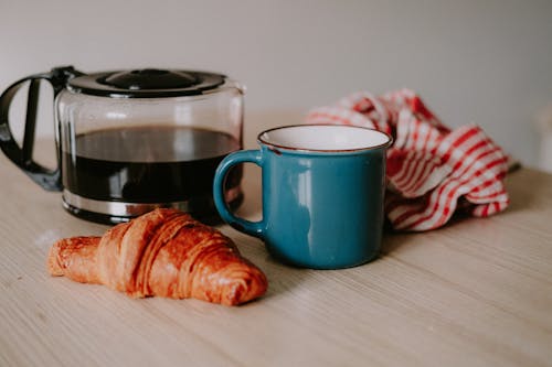 
A Croissant beside a Coffee Pot and a Mug